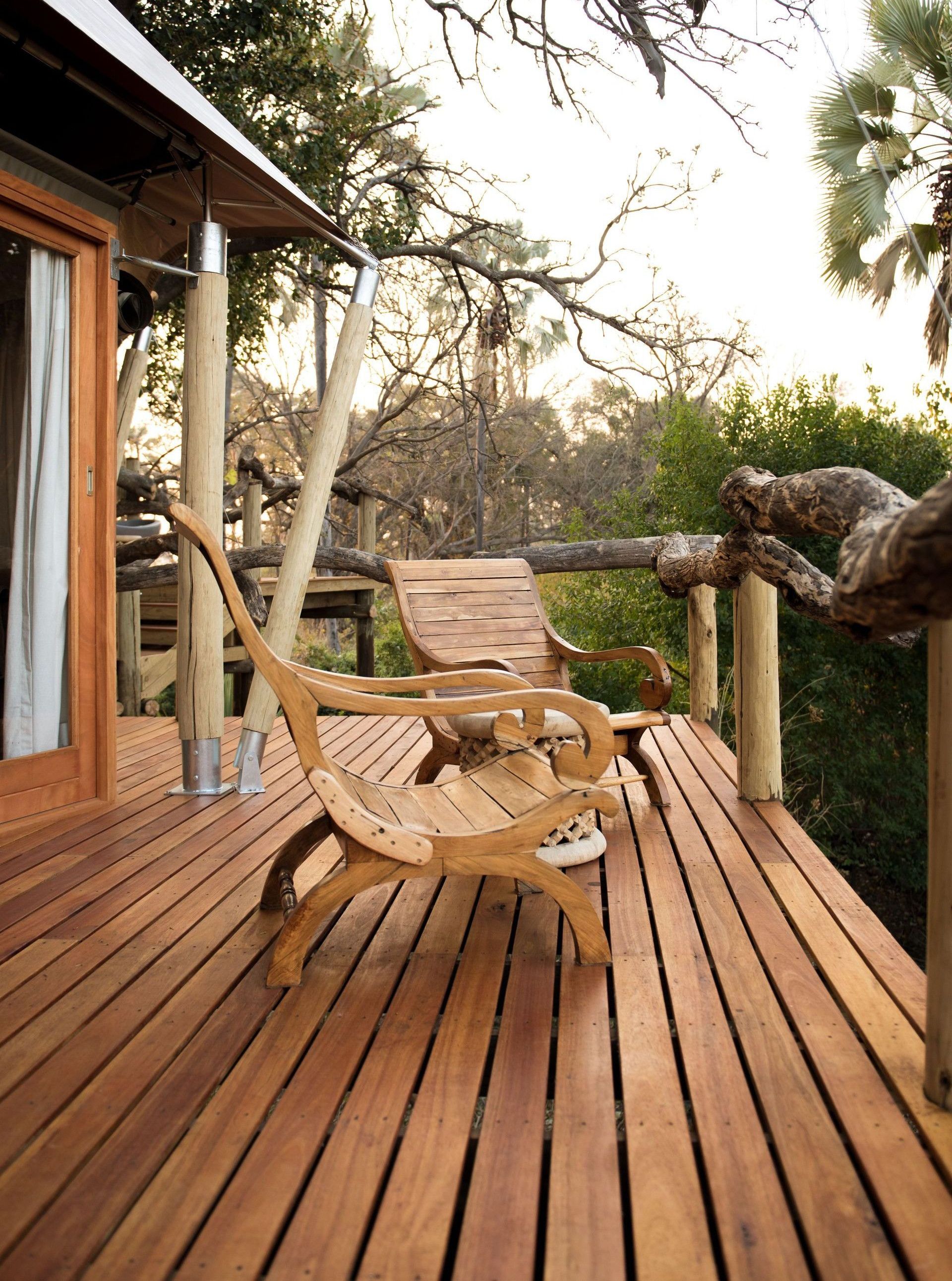 Two wooden chairs on a rustic deck surrounded by lush nature.