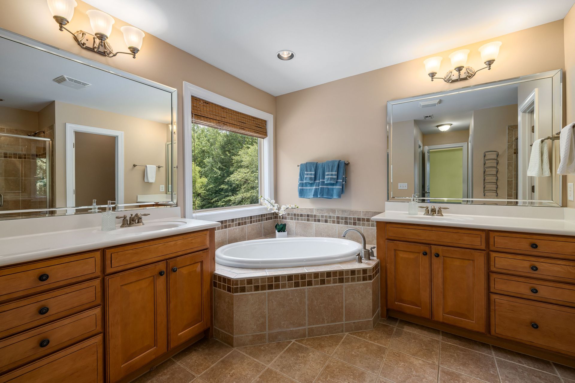 Contemporary bathroom design featuring a corner bathtub, wooden cabinets, and large mirrors.