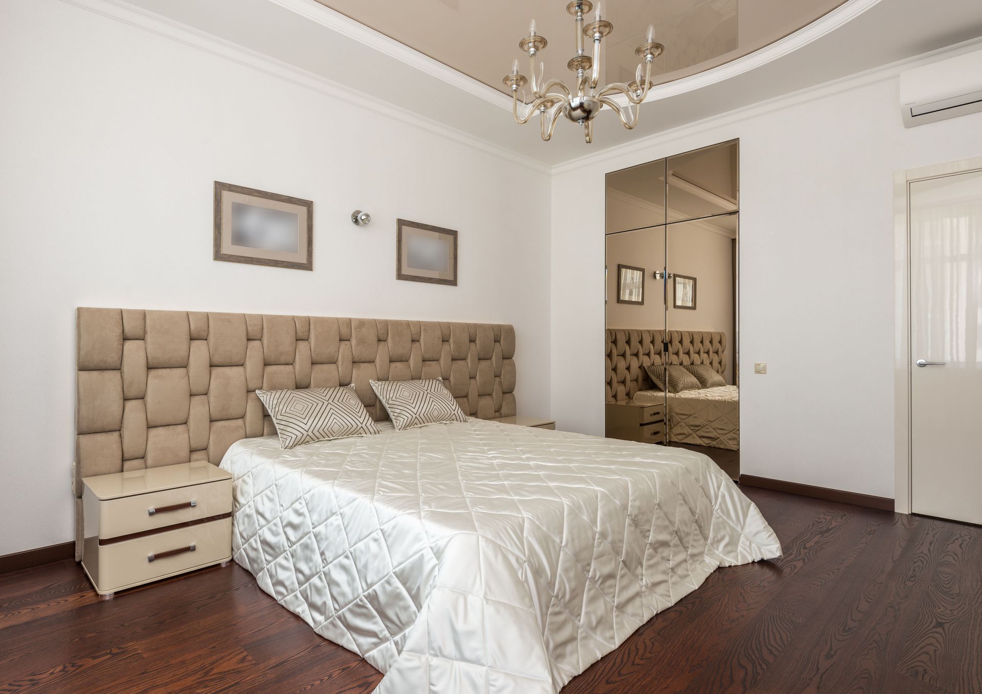 Stylish modern bedroom with plush headboard, chandelier, and mirrored closet doors.